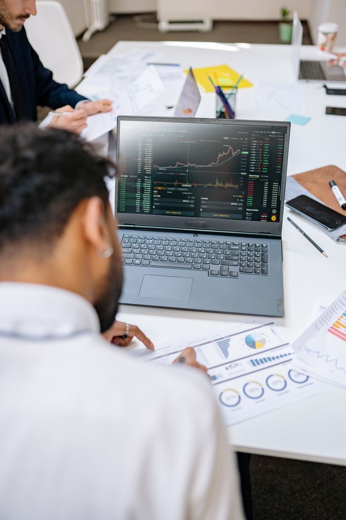 Business professionals analyzing stock charts and graphs on a laptop in an office setting.